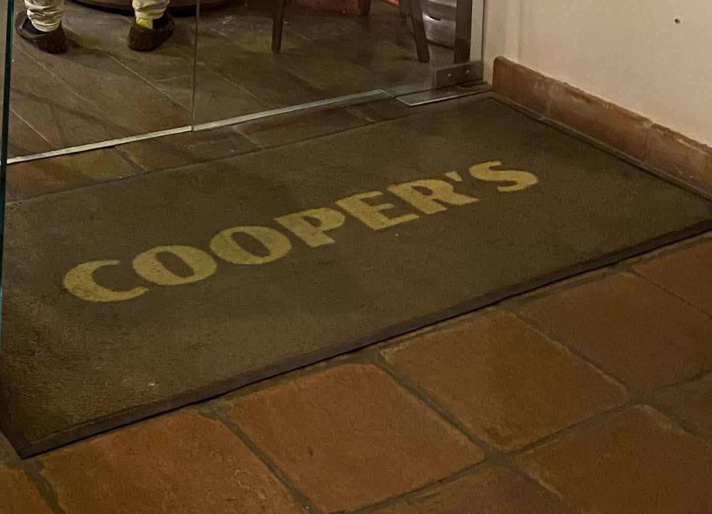 Felpudo con el nombre «Cooper's» en la puerta de cristal del pub, en el centro de Estepona.