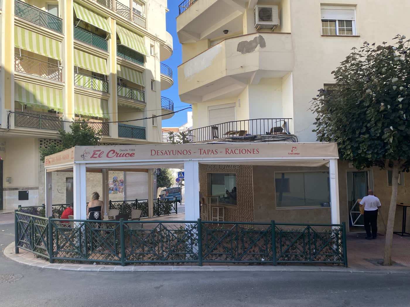 Terraza del Bar El Cruce en la calle Tajo de Estepona, con su toldo «Desde 1988 · Desayunos · Tapas · Raciones».