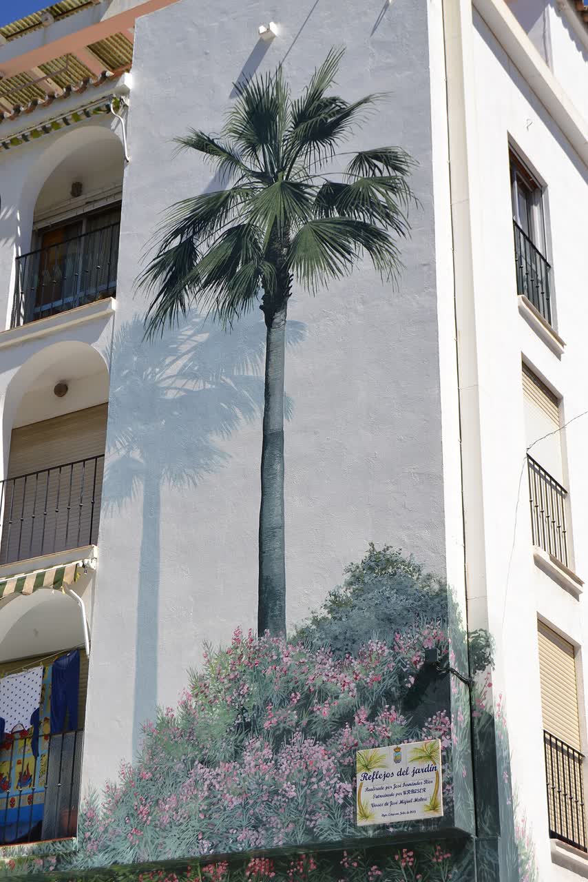 Mural «Reflejos del jardín»: fachada pintada con palmeras, buganvillas y balcones junto al Orquidario de Estepona.